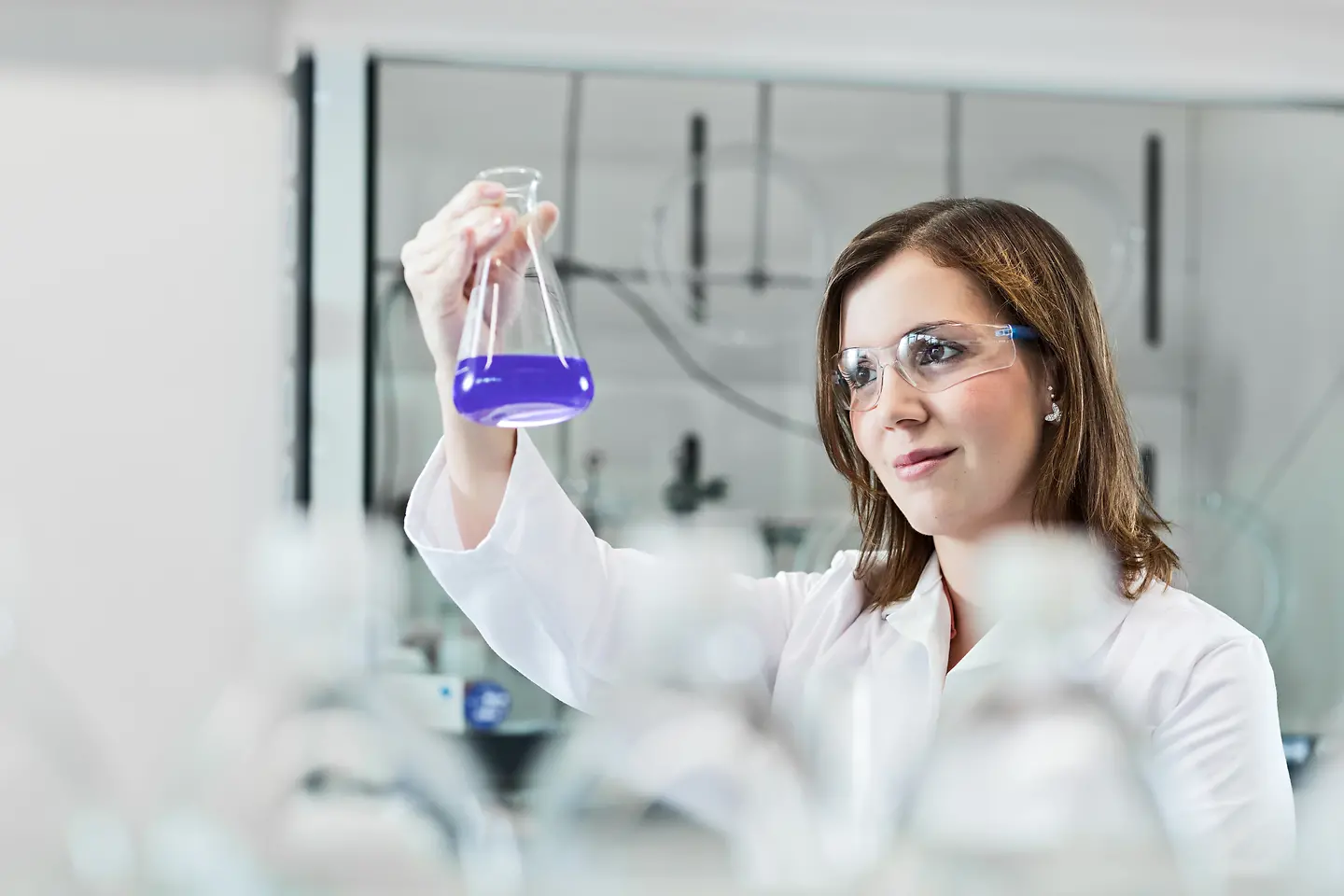 A female scientist is experimenting in a lab, wearing a lab coat and safety goggles.