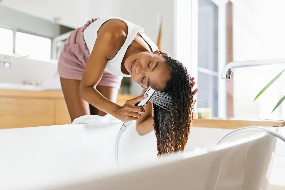 Mujer en el baño lavado su largo cabello castaño en la bañera.