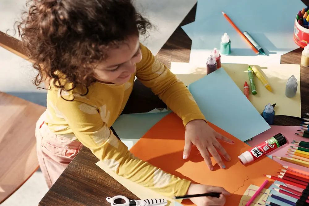 Niño haciendo artesanías usando pegamento en barra marca Pritt.